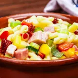 Leckerer nudelsalat ohne mayonnaise mit bunten Paprikawürfeln, Schinken und Frühlingszwiebeln in einer Tonschüssel.