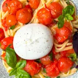 Ein cremiger Burrata Salat mit Pasta, Kirschtomaten und Basilikum auf einem gemusterten Teller.