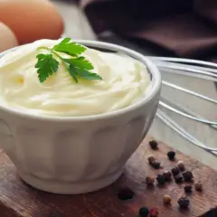 Frische Eier und Petersilie auf einem Holzbrett, bereit, um köstliche Mayonnaise selber machen. Ein Schneebesen liegt daneben.