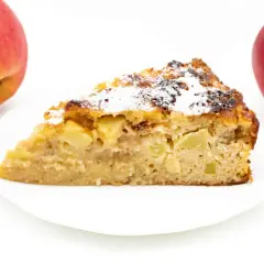 Ein Stück Apfelkuchen ohne Zucker mit Quark, bestäubt mit Puderzucker. Zwei Äpfel liegen daneben.