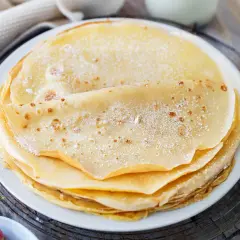 Ein Stapel goldbrauner Pfannkuchen, bestäubt mit Puderzucker. Daneben Schüsseln mit Blaubeeren und Erdbeeren. Ein sehr gutes Pfannkuchen Rezept für den Genuss.