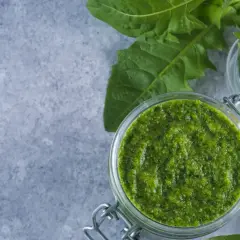 Frisches Löwenzahnpesto im Glas, bereit zum pesto haltbar machen. Daneben Walnüsse und Löwenzahnblüten.