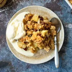 Ein Teller mit warmem Apfelcrumble und einer Kugel cremigem Vanilleeis, bestäubt mit Puderzucker.
