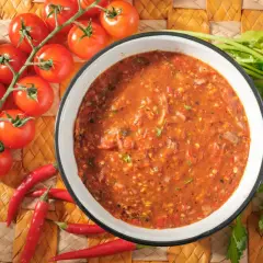 Schüssel mit würziger Salsa Brava, daneben frische Tomaten, Knoblauch und Chilischoten. Perfekt für Ihr nächstes salsa brava rezept!