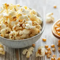 Frisch zubereiteter popcorn im topf, dane Maiskörner auf einem Holzlöffel.