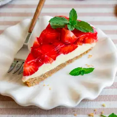 Ein Stück Erdbeerkuchen mit Frischkäsefüllung und glasierten Erdbeeren, garniert mit Minze. Perfekt für einfache Desserts ohne Backen.