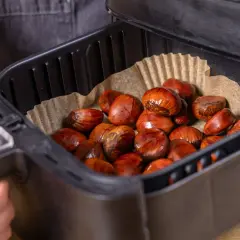 Maronen im Airfryer, bereit für die Zubereitung. Die braunen, glänzenden Früchte liegen auf Backpapier in dem schwarzen Korb.
