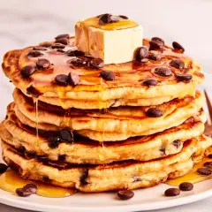 Ein Stapel saftiger Schokoladensplitter-Pfannkuchen, übergossen mit Ahornsirup und einem Stück Butter.