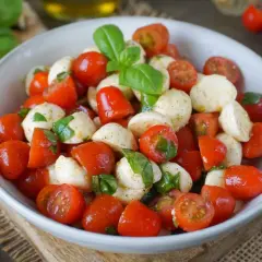 Ein frischer italienischer Salat mit Kirschtomaten, Mozzarella-Bällchen und Basilikumblättern, appetitlich in einer Schüssel angerichtet.