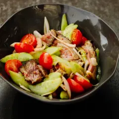 Ein herzhafter Yam Nua Salat mit gegrilltem Rindfleisch, Tomaten und Gurken in einer dunklen Schüssel.