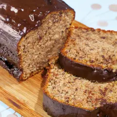 Ein **super saftiger Bananenkuchen** mit Schokoladenglasur, angeschnitten auf einem Holzbrett.