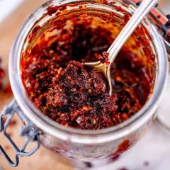 Ein Glas mit selbstgemachtem, würzigem Chiliöl. Ein Löffel hebt die glänzende, rote Masse hervor, perfekt für jedes crispy chili oil rezept.