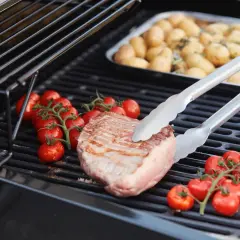 Duroc secreto zubereitung: Ein saftiges Steak wird mit Kirschtomaten auf dem Grill zubereitet. Daneben liegen Kartoffeln in einer Schale.