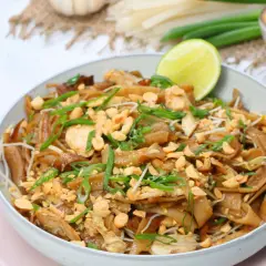 Schüssel mit Pad Thai Gai, garniert mit Erdnüssen und Frühlingszwiebeln, dazu eine Limettenspalte.