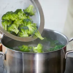 Frischer Brokkoli wird in einem Sieb über einem Topf mit kochendem Wasser gehalten, bereit zum Blanchieren.