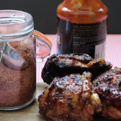 Glas mit Gewürzmischung, perfekt für ein magic dust rezept. Daneben saftige, gegrillte Hähnchenteile und eine Flasche BBQ-Sauce.