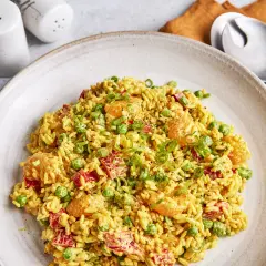 Ein Teller mit weltbestem Reissalat mit Curry, garniert mit Erbsen, Paprika und Frühlingszwiebeln.