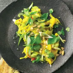 Ein bunter, frischer Mango Salat Thai mit Erdnüssen und Kräutern auf einem dunklen Teller.