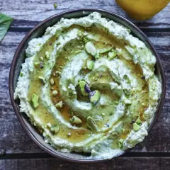 Cremiges Avocado Basilikum Pesto mit Pistazien und Honig beträufelt, garniert mit frischen Basilikumblättern und Zitronenspalten.