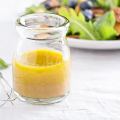 Ein Glas mit gelber Vinaigrette, daneben ein Schneebesen. Ein einfaches vinaigrette rezept für frische Salate.