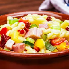 Leckerer nudelsalat ohne mayonnaise mit bunten Paprikawürfeln, Schinken und Frühlingszwiebeln in einer Tonschüssel.