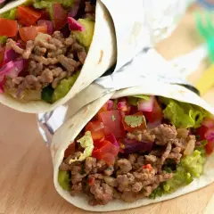 Zwei saftige wraps mit hackfleisch, Guacamole, Tomaten und roten Zwiebeln, eingewickelt in Folie.
