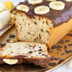 Saftiger Bananen Buttermilch Kuchen mit Schokoladenglasur und Bananenscheiben, garniert mit Schokostückchen.