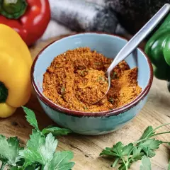 Schüssel mit Gewürzmischung, perfekt zum pul biber selbst mischen. Bunte Paprika und frische Petersilie liegen daneben.