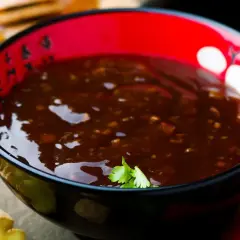 Eine Schüssel mit glänzender Teriyaki-Sauce, umgeben von Ingwer und braunem Zucker. Was ist Teriyaki? Eine süß-salzige Glasur für Fleisch und Fisch.