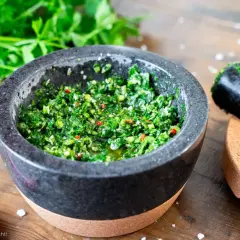 Frisches Chimichurri-Rezept im Mörser, bereit zum Verfeinern von Grillgut. Kräuter, Chili und Öl duften verführerisch.