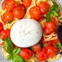 Ein cremiger Burrata Salat mit Pasta, Kirschtomaten und Basilikum auf einem gemusterten Teller.