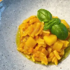 Herzhaftes Pasta e Patate mit Kartoffelstücken, Nudeln und frischem Basilikum in Olivenöl, serviert in einer grauen Schale.