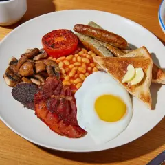 Ein üppiges **full English breakfast** mit Spiegelei, Speck, Würstchen, Bohnen, Pilzen, Tomate, Blutwurst und Toast.