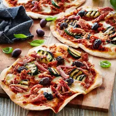 Drei kleine Pizzen mit pulled pork, gegrillter Zucchini und Oliven auf einem Holzbrett.