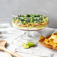 Schicht für Schicht ein Genuss: Ein bunter 7-Layer-Dip in einer Glasvitrine, bereit zum Dippen mit Tortilla-Chips.