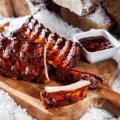 Saftige rippchen im backofen, glasiert und mit BBQ-Sauce, auf einem Holzbrett mit Schnee dekoriert.