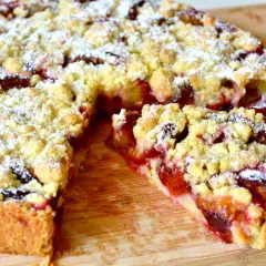 Omas Pflaumenkuchen aus Hefeteig in Springform, mit Streuseln und Puderzucker bestäubt. Ein Stück ist herausgeschnitten.