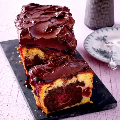 Saftiger Marmorkuchen mit Kirschen und dunkler Schokoladenglasur, auf einem schwarzen Brett serviert.