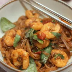 Pad Kee Mao mit Garnelen, Reisnudeln, Basilikum und Tomaten in einer Schüssel, bereit zum Genießen.
