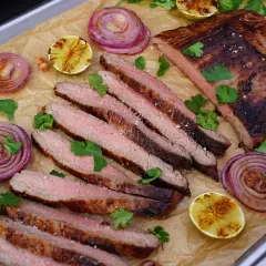 Saftiges bavette d'aloyau rezept: gegrilltes Steak, perfekt geschnitten, mit gerösteten Zwiebeln, Limetten und Koriander garniert.