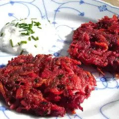 Zwei knusprige rote Bete Puffer paniert, serviert mit einem Klecks Kräuterquark auf einem Teller mit blauem Muster.