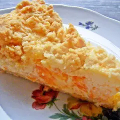 Ein Stück Mandarine Schmand Kuchen mit Streuseln auf einem Teller mit Blumenmuster.