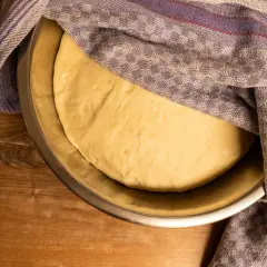 Frischer, aufgegangener Teig für pizzateig selber machen ruht in einer Schüssel unter einem karierten Tuch.