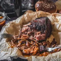 Pulled Pork aus dem Airfryer, saftig und zart, mit BBQ-Sauce beträufelt. Dazu passen die aufgeschnittenen Burgerbrötchen.