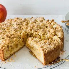 Ein saftiger, bester Apfelkuchen mit Streusel, bereit zum Servieren. Daneben liegen rote Äpfel.
