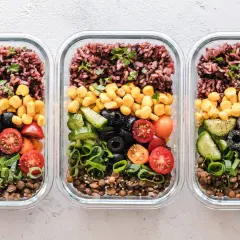 Drei Glasbehälter mit Linsen, Gurken, Tomaten, Oliven, Mais und braunem Reis – tolle meal prep ideen für gesunde Mahlzeiten.
