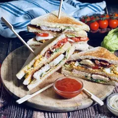 Drei saftige Club Sandwiches mit Hähnchen, Speck, Ei und Tomaten, serviert mit Ketchup und Mayo.