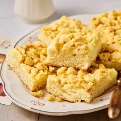 Saftiger Apfelkuchen vom Blech mit knuspriger Streuselhaube auf einem Teller, daneben botanische Apfelzeichnungen.