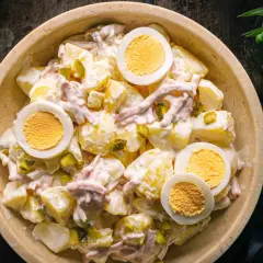 Schüssel mit Kartoffelsalat und Fleischsalat, garniert mit hartgekochten Eiern und Gewürzgurken.