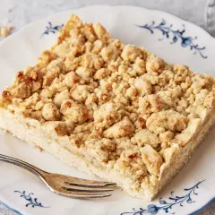 Ein Stück Streuselkuchen, wie von Oma nach DDR-Rezept, mit knusprigen Streuseln auf einem Teller mit blauem Rand.